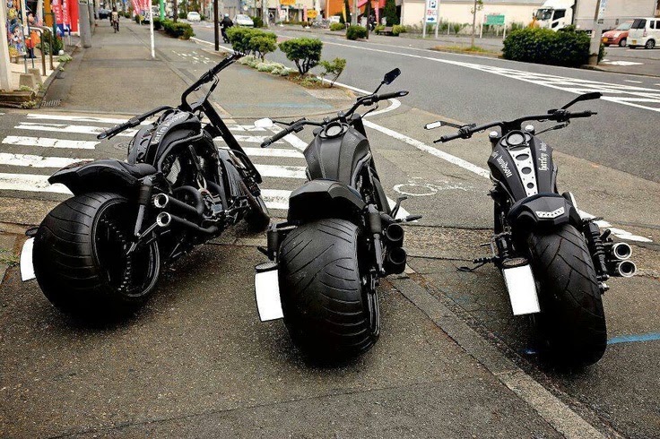 Three black custom motorcycles parked at a curb